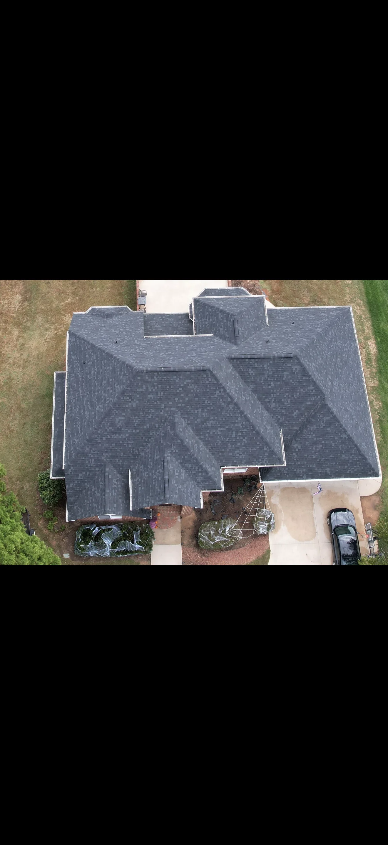 Aerial view of completed residential roof replacement with charcoal gray shingles and white trim