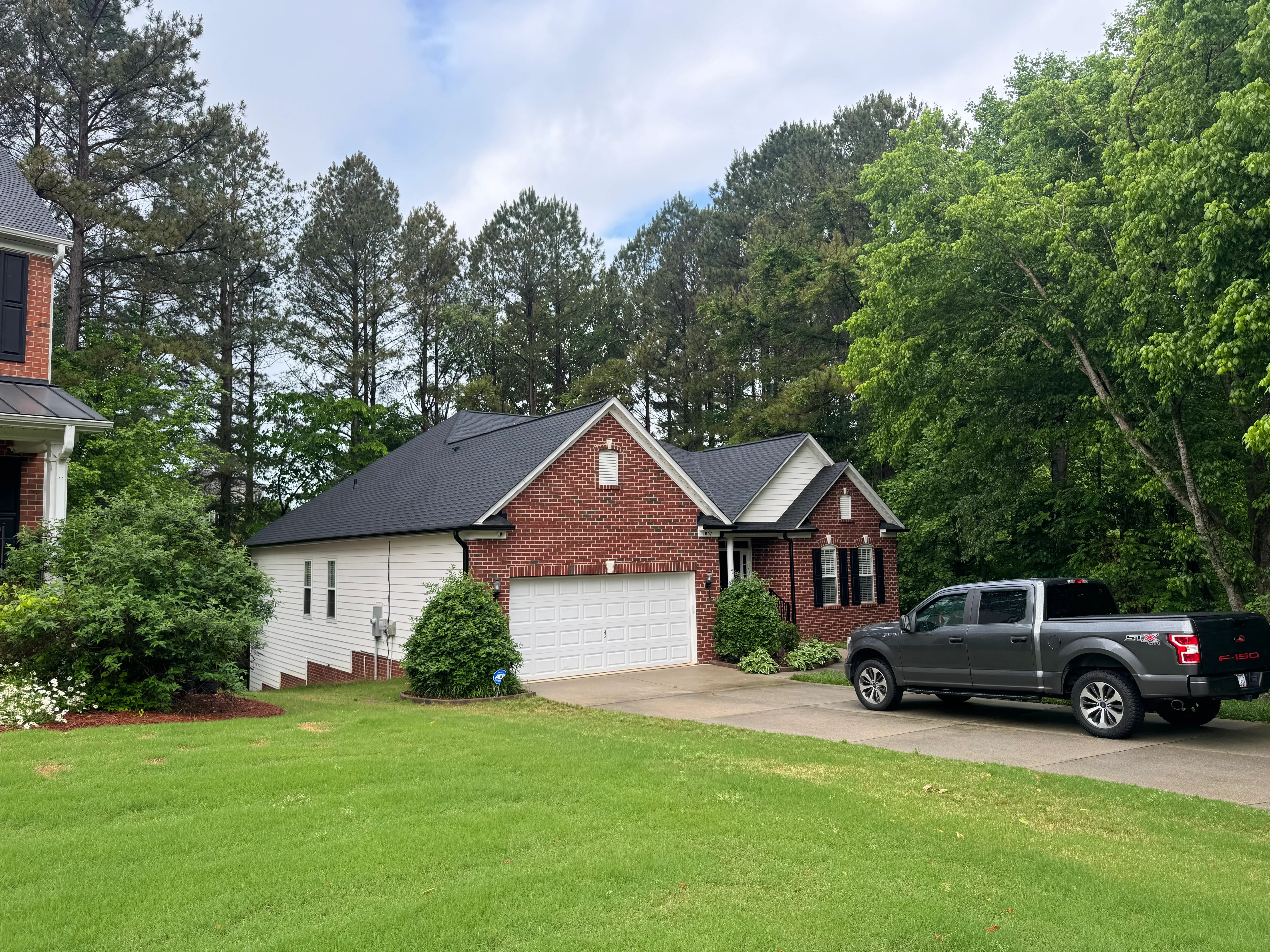 Brick home with new charcoal gray asphalt shingle roof in wooded residential setting